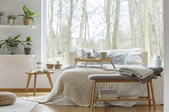 Calm white bedroom with plants and large window with view of trees.