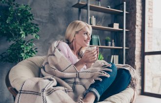 Women snug and warm sat on chair with hot drink